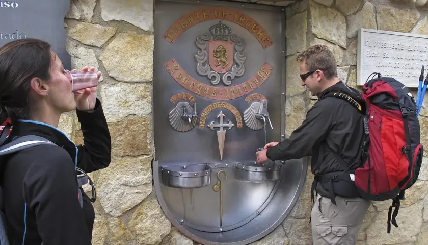Peregrinos en el Camino de Santiago se refrescan en la fuente del vino y agua de Irache.