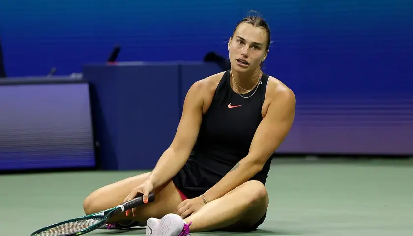 Zmęczona tenisistka siedzi na korcie, trzymając rakietę. Intensywny mecz tenis kobiet.