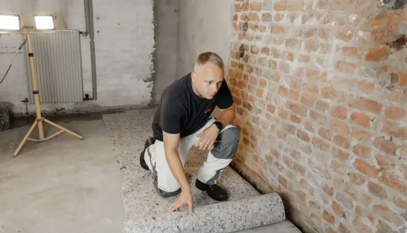 Mann verlegt Dämmmaterial auf dem Boden im Keller, um den **bodenbelag keller feucht** zu schützen.