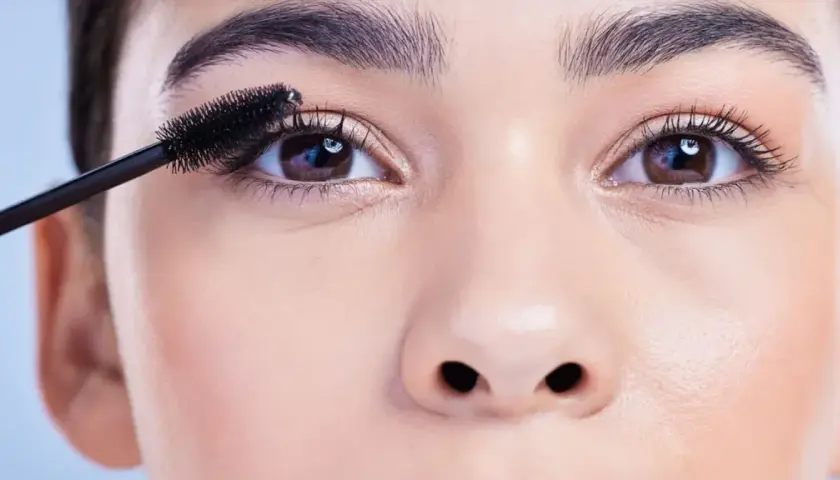 Eine Hand trägt Mascara auf die Wimpern auf, um runde Augen zu schminken.