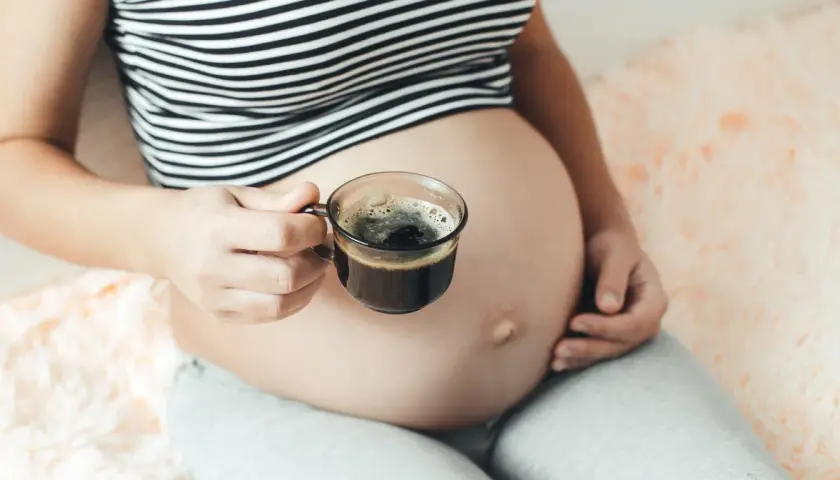 Kobieta w ciąży trzyma filiżankę kawy. Delikatny napój dla przyszłych mam.