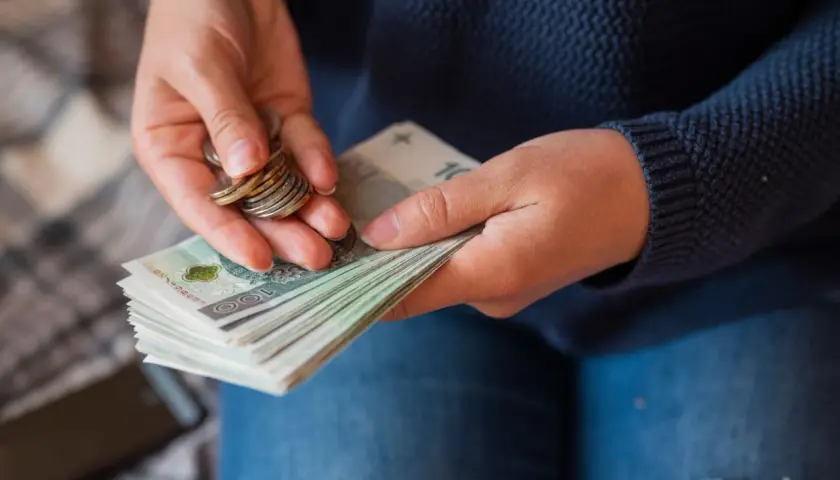 Dłonie liczą banknoty i monety, przygotowując się do wypłaty pensji.