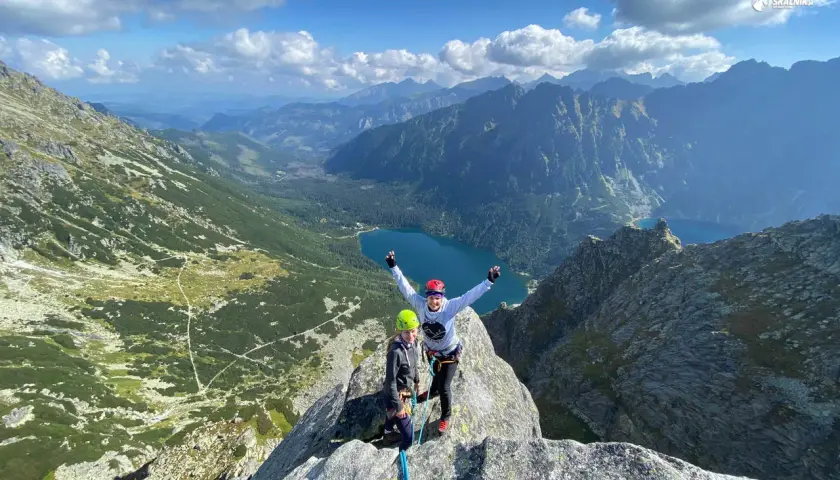 Dwóch wspinaczy na szczycie, radość po udanej wspinaczce. W tle malownicze Tatry i jezioro.