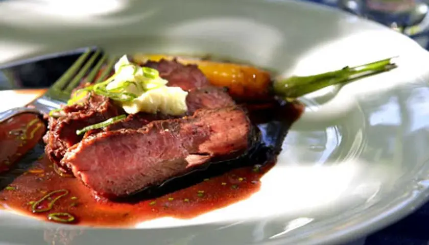 Skivad flat iron steak med perfekt medium-rare temperatur, serverad med en mustig sås och garnering.
