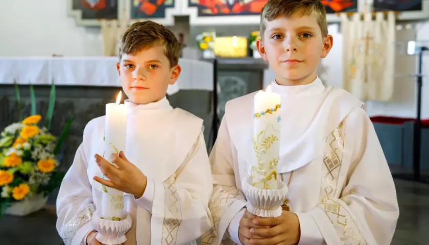 Dwóch chłopców w albach trzyma świece. Czy do komunii może być świeca od chrztu? Ta ozdobna świeca wygląda jakby mogła być użyta na obu uroczystościach.