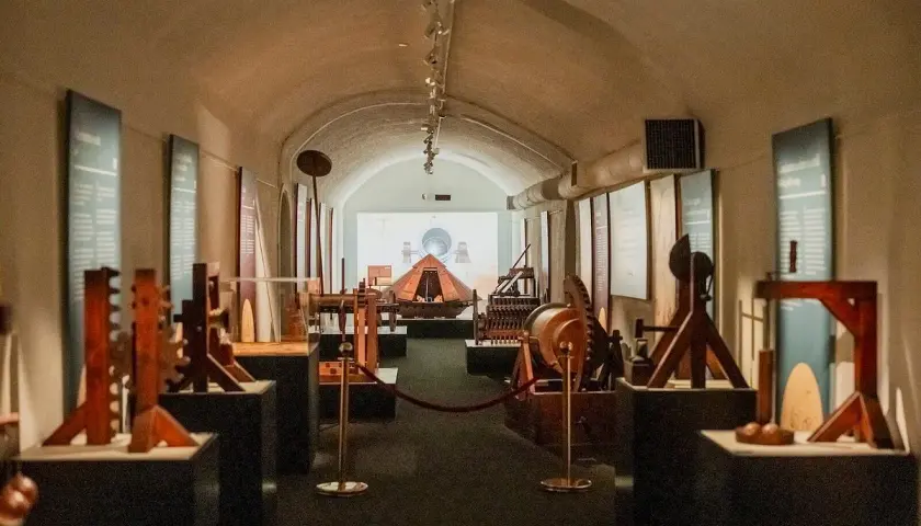 Maquettes d'inventions de Léonard de Vinci exposées dans un couloir voûté, une invitation à explorer le musée Léonard de Vinci à Rome.