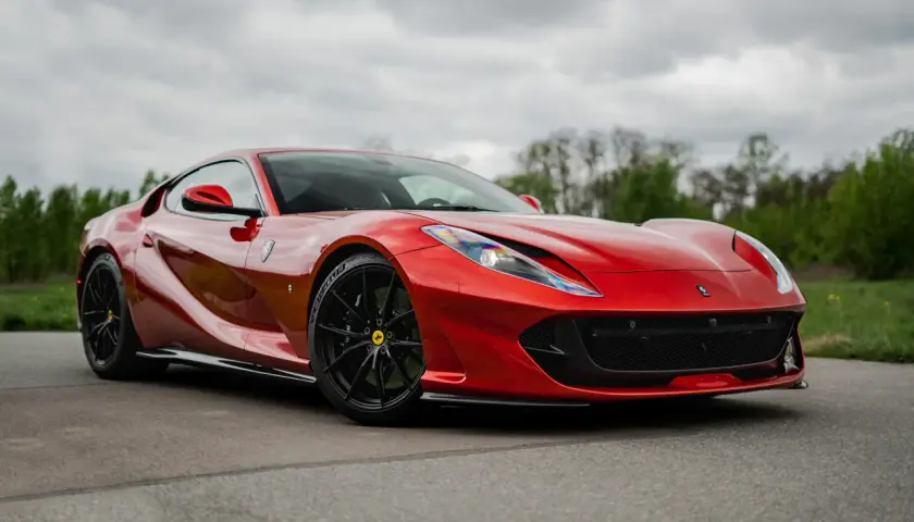 Czerwone, ładne auta sportowe Ferrari na tle zieleni i chmur.