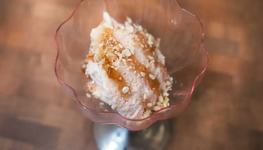 En skål med rosa rabarbersorbet toppad med nötter och sirap. En härlig sommardessert.