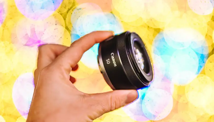 Dłoń trzyma obiektyw Canon 50mm na tle kolorowych świateł bokeh.