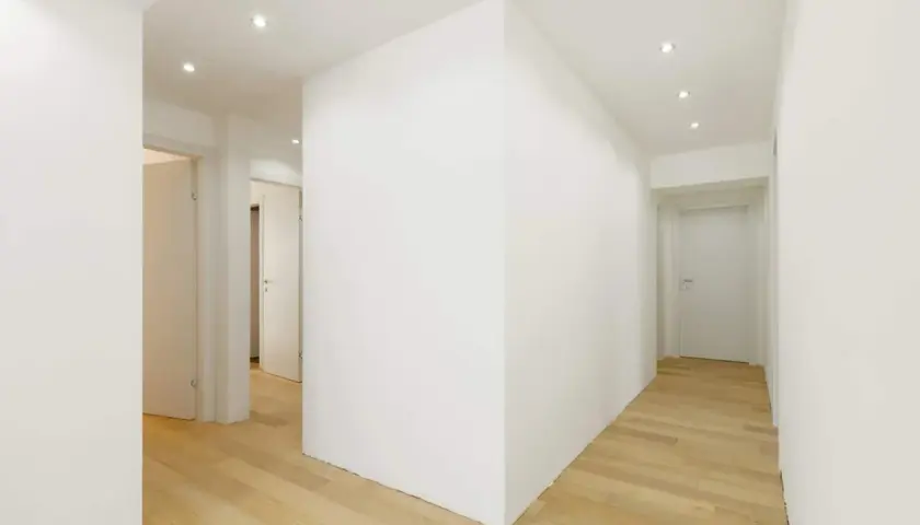Un corridoio moderno con pavimenti in legno chiaro e una parete in cartongesso curvo che crea un effetto dinamico.