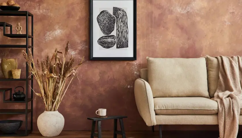 Rusty, textured wall – świetny pomysł co na ścianę zamiast farby. Obok kanapa, grafika i suszone trawy.