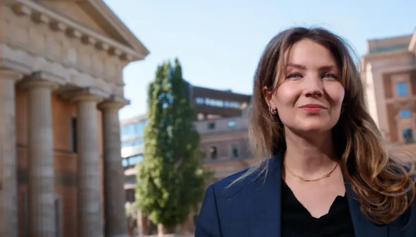 Cecilia Khavar ler mot kameran framför en klassisk byggnad med pelare.