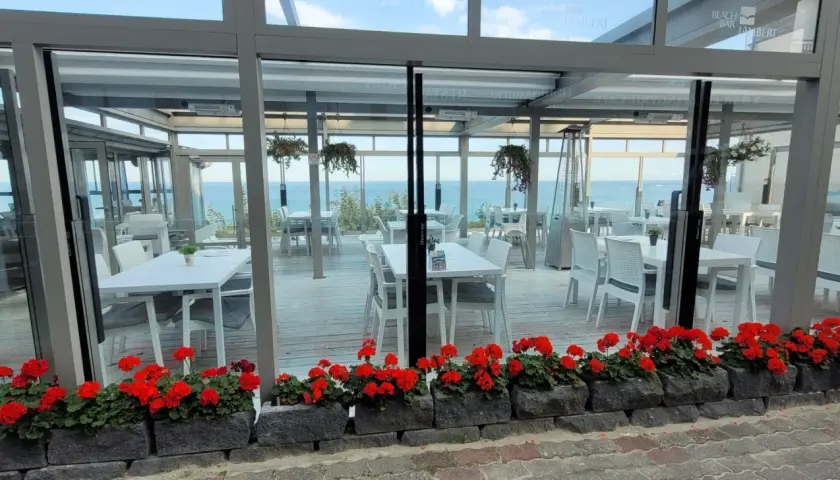 Letnia atmosfera przy plaży w Hotelu Lambert. Stoliki i krzesła czekają na gości, a morze w tle zaprasza do relaksu.