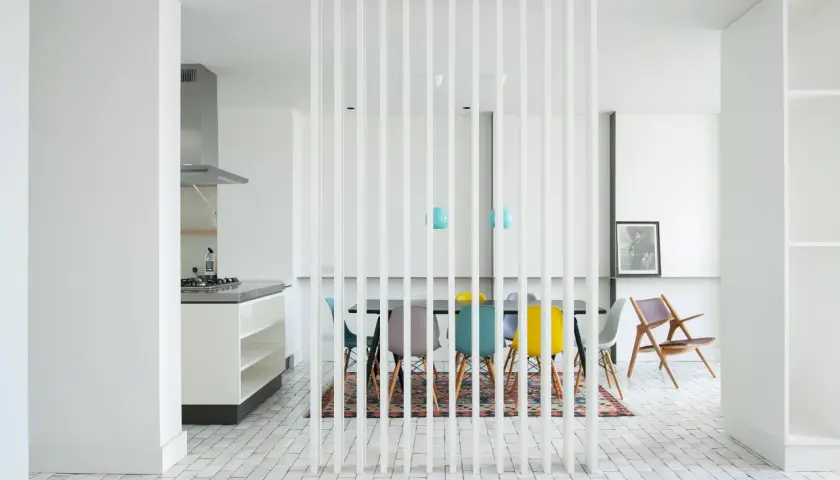 Un divisorio a listelli bianchi separa la cucina moderna da una zona pranzo con sedie colorate. Un'idea per come riempire spazio tra cucina e muro.