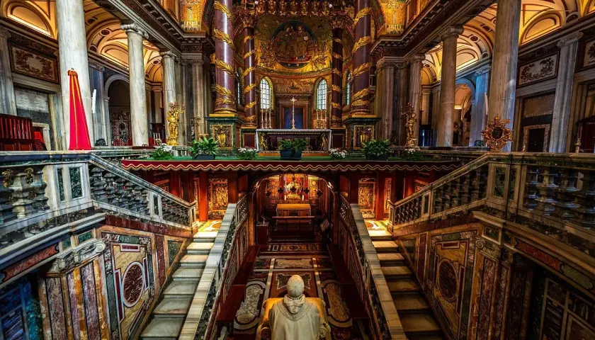 Interno della chiesa San Pietro a Roma, con scale marmoree, mosaici dorati e un altare imponente.