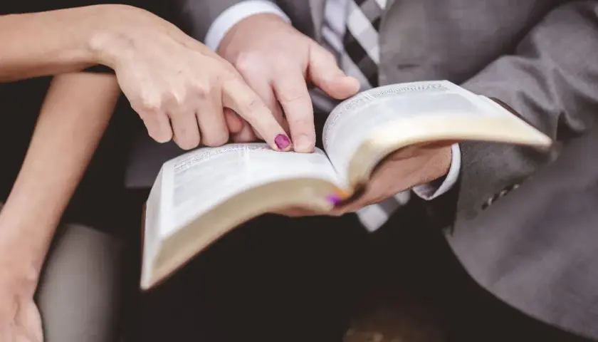 Dłonie pary wskazują na tekst w Biblii, symbolizując wspólną drogę i ewangelia na ślub.
