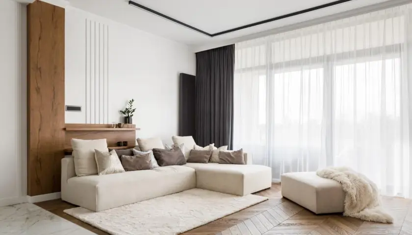 Nowoczesny salon z beżową sofą i puszystym dywanem. Elegancki karnisz do zabudowy dyskretnie podkreśla zasłony.