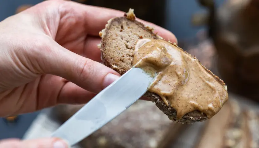 Mano spalma crema di nocciole su pane integrale. Ottima per conoscere i crema di nocciole valori nutrizionali.