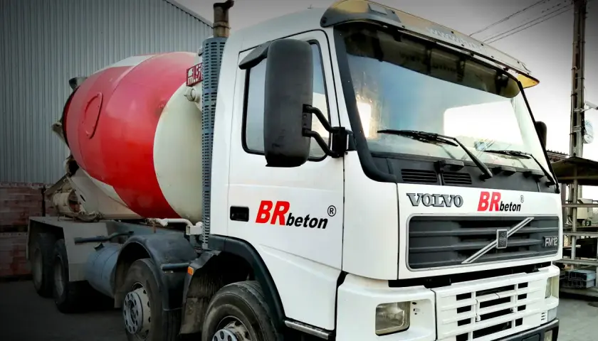Biała ciężarówka Volvo z czerwoną obrotową beczką na beton. To jeden z rodzajów betoniarek, gotowy do transportu budowlanego.