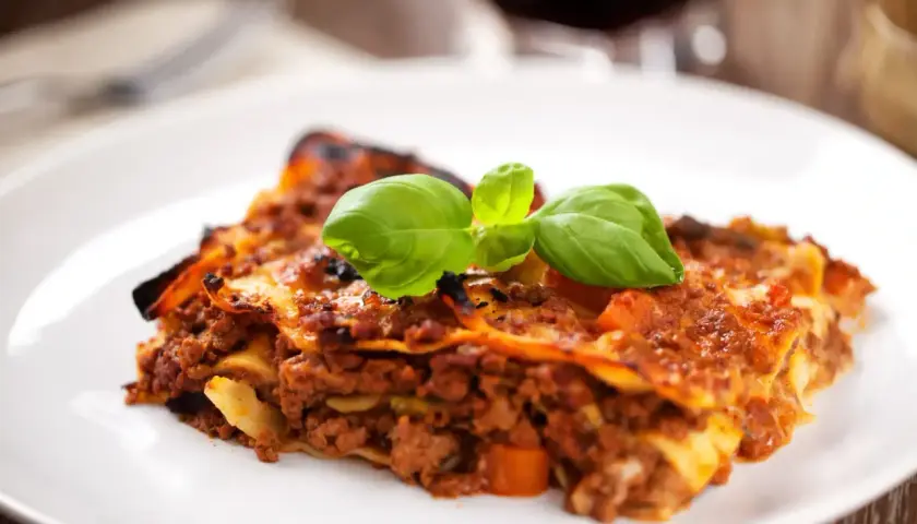 Une part de lasagnes à la bolognaise, garnie de basilic frais. Un plat réconfortant, parfait avec un verre de vin rouge. Quel vin avec des lasagnes ?