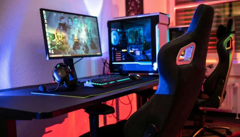 Gaming-Setup mit beleuchtetem PC, Tastatur und Kopfhörern. Der **Atlas OS**-Desktop zeigt ein Spiel.