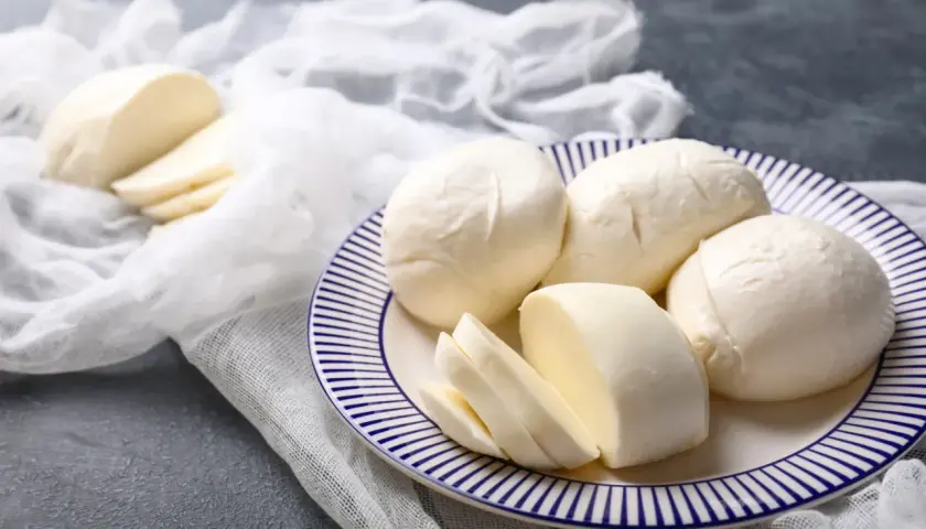 Świeża mozzarella na talerzu, pokrojona i w całości. Czy mozzarella podnosi cukier? Ten ser jest niskowęglowodanowy.