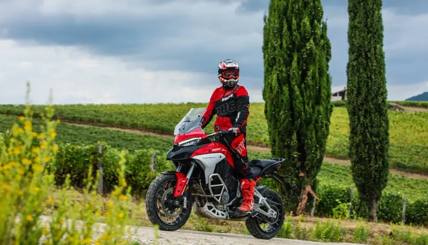 Un motociclista in tuta rossa sfreccia tra i vigneti toscani, godendosi le strade più belle della Toscana in moto.
