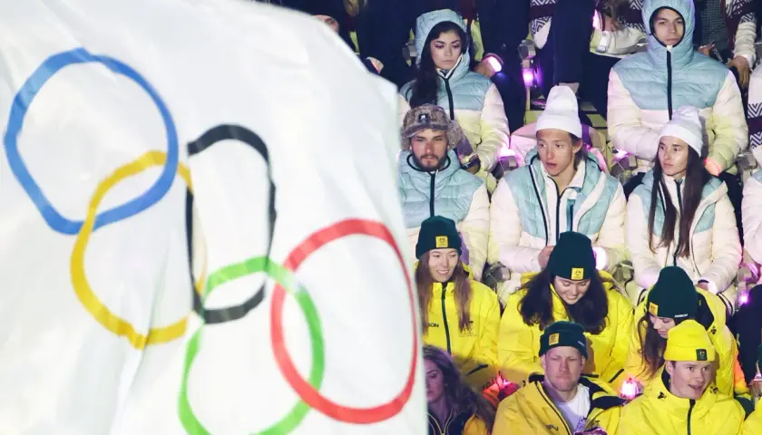 Młodzi sportowcy w barwach narodowych, z flagą olimpijską w tle, czekają na start reprezentacji Polski na Zimowe Igrzyska Olimpijskie 2026.