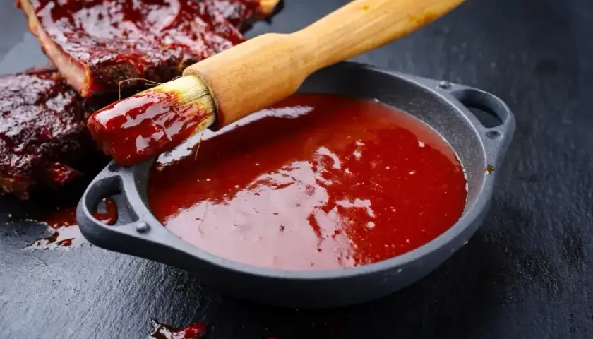 Pędzel z sosem barbecue zanurzony w miseczce, obok żeberka. Idealny sposób, jak zrobić sos barbecue.