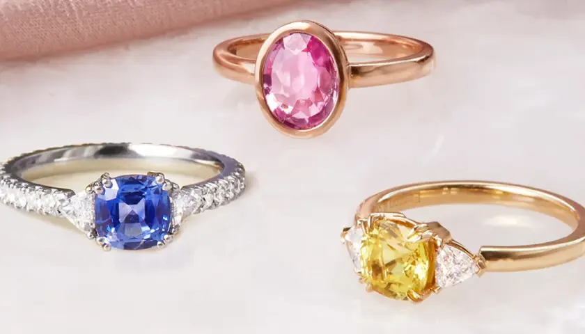 Drei Ringe mit Edelsteinen: ein blauer Saphir, ein gelber Saphir und ein rosa Saphir. Die Bedeutung von rosa Saphir steht für Liebe und Mitgefühl.