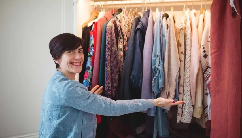 Une femme souriante devant une penderie remplie de vêtements colorés. Elle semble hésiter, car je n'arrive pas à jeter mes vêtements.