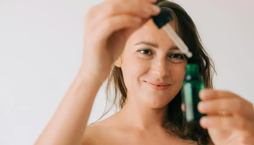 Kobieta z piegami trzymająca pipetkę z zieloną buteleczką.
