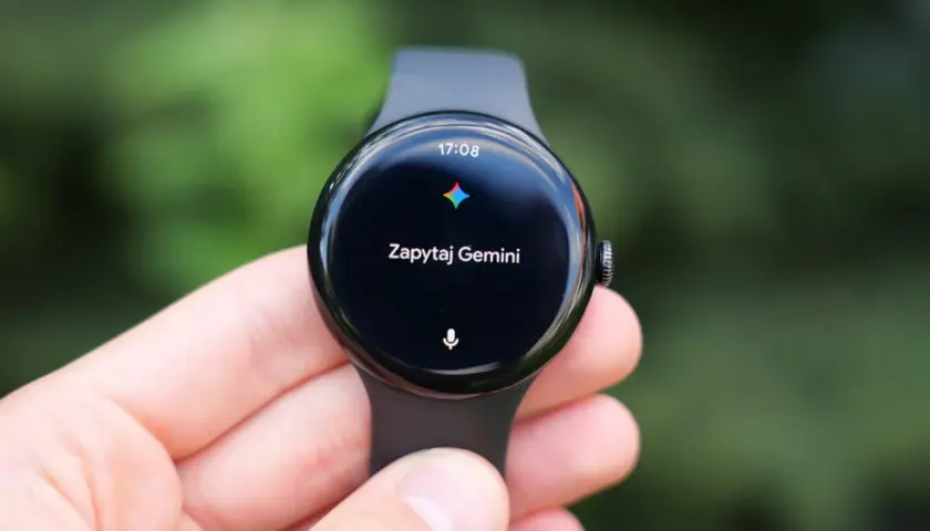 Zegarek z Wear OS na ręce, wyświetla godzinę 17:08 i komunikat "Zapytaj Gemini".