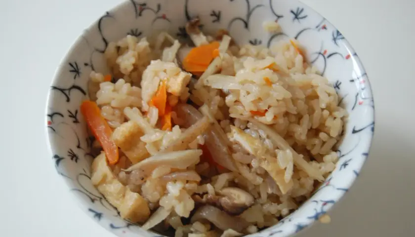 A bowl of gomoku rice, a Japanese mixed rice dish, filled with fluffy rice, tender carrots, shiitake mushrooms, and fried tofu.