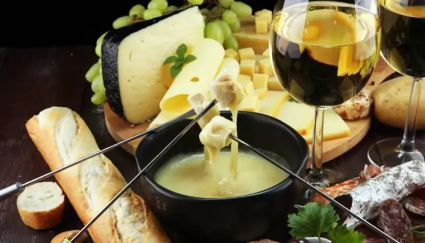 Un délicieux vin accompagne une fondue au fromage, avec du pain, des pommes de terre et de la charcuterie.