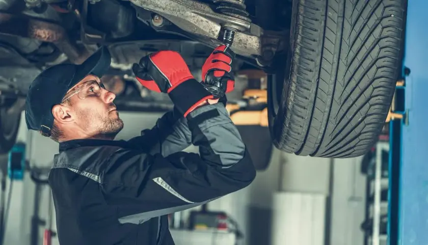 Mechanik w rękawiczkach dokręca sworzeń wahacza kluczem nasadowym pod podniesionym samochodem.