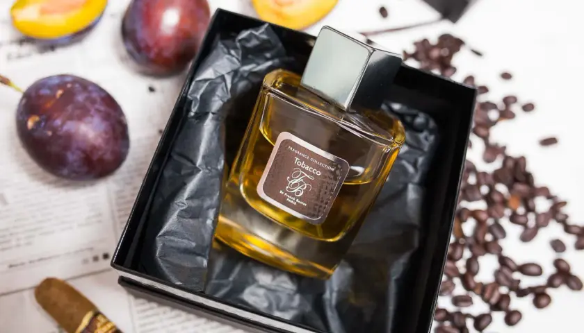 Perfumy "Tobacco" by Franck Boclet w eleganckim flakonie, otoczone śliwkami, kawą i cygarem.