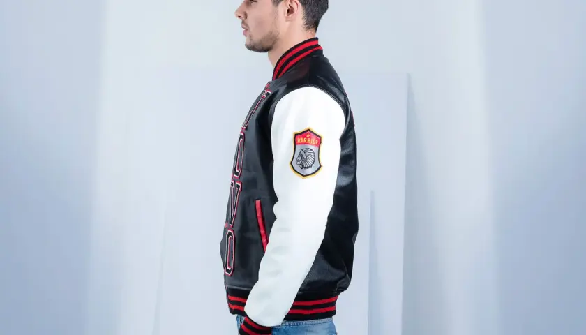Man in profile wearing a black and white letterman jacket with red trim and a "Warrior" patch.