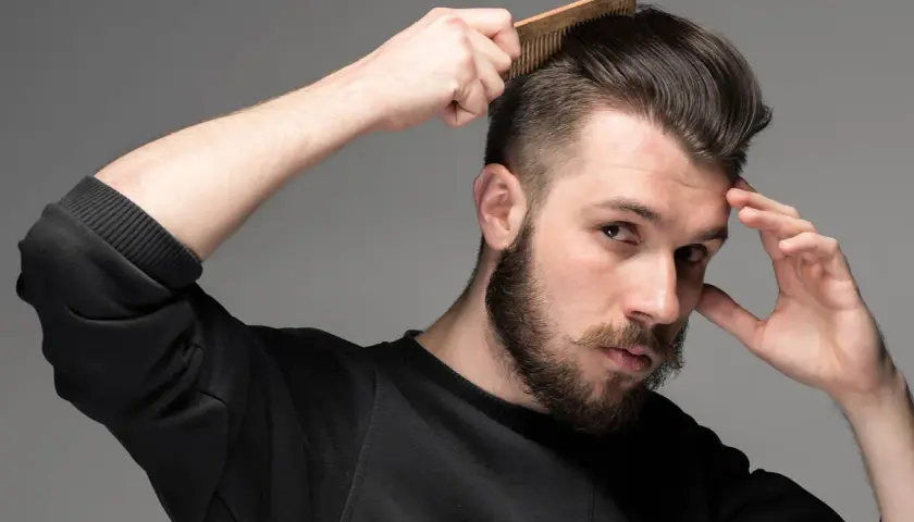 Man med skägg och mustasch kammar sitt hår som har en snygg taper fade.