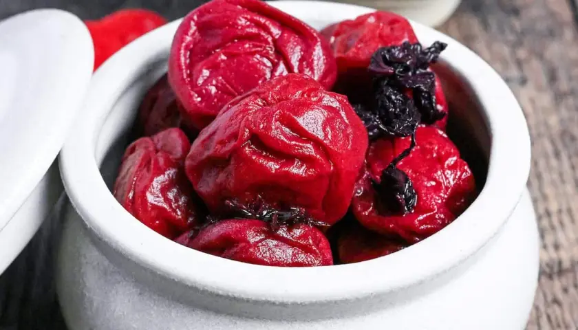 A white ceramic bowl filled with glistening, deep red umeboshi plums, ready for a delicious umeboshi recipe.