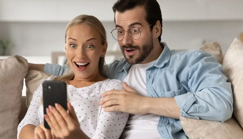 Para ogląda na telefonie, śmiejąc się z głupich pytań. Ich miny wyrażają zdziwienie i rozbawienie.