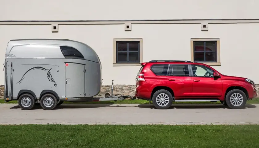 Czerwony SUV ciągnie przyczepę z wizerunkiem konia.