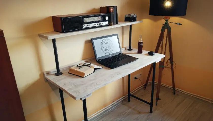 Stylowe biurko z palet, z laptopem, książką i okularami, dopełnione lampą i radiem retro.