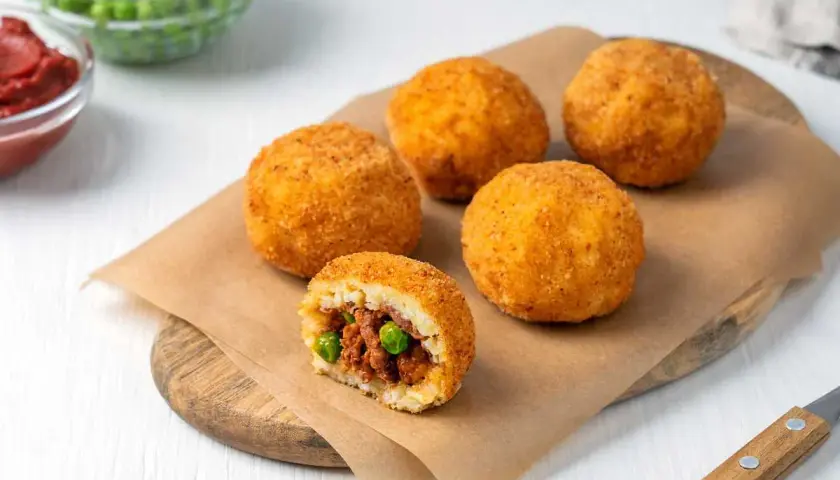 Arancini dorados y crujientes, uno cortado revela un relleno de carne y guisantes. ¡Una deliciosa receta arancini lista para disfrutar!