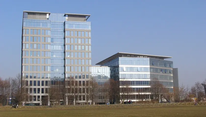 Nowoczesne budynki Olivia Tower i sąsiedni biurowiec z przeszklonymi fasadami, na tle błękitnego nieba.