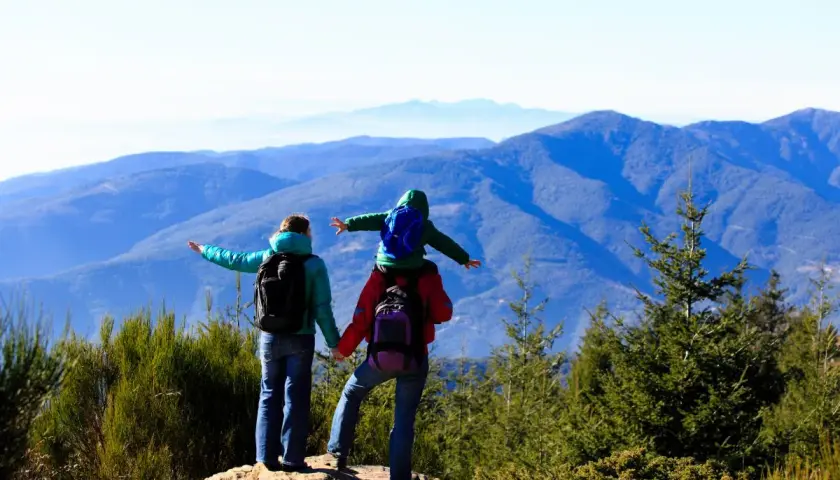 Familia disfrutando de las rutes montseny, con un niño a hombros, contemplando el paisaje montañoso.