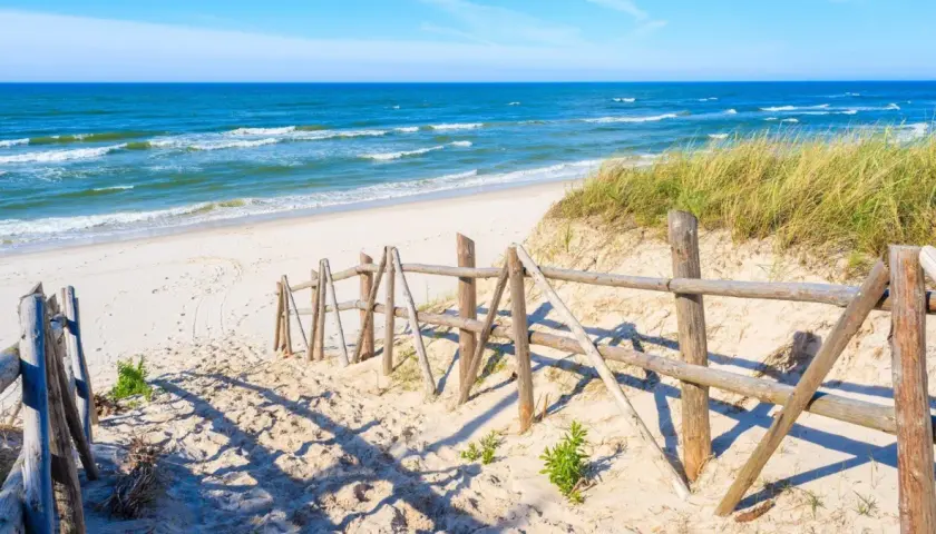 Piękna plaża w Łebie, idealne miejsce na spacer. Drewniane płotki prowadzą do morza, a trawy na wydmach dodają uroku.