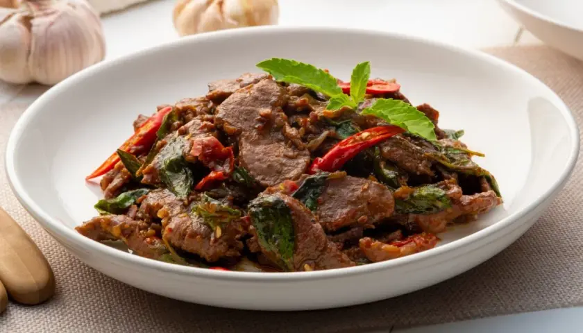 Aksamitne kawałki wołowiny po tajsku z bazylią i papryczką chili, podane w białej misce.