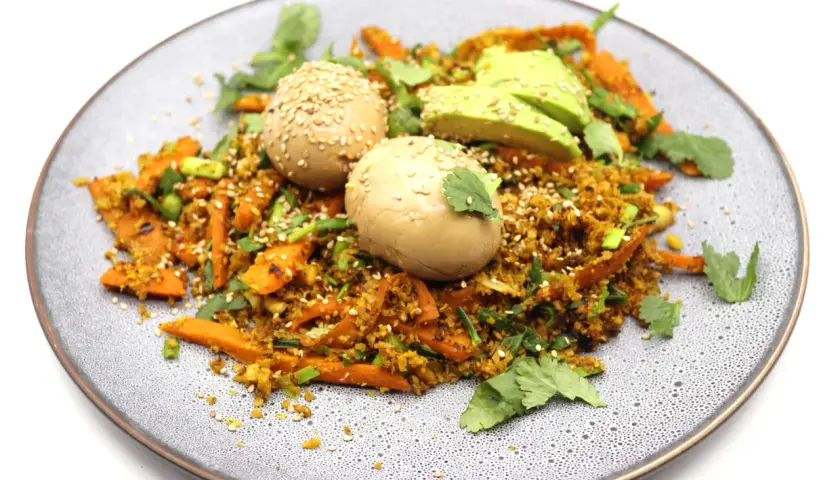 Assiette de riz aux légumes et deux oeufs marinés japonais, parsemée de graines de sésame et de coriandre fraîche.