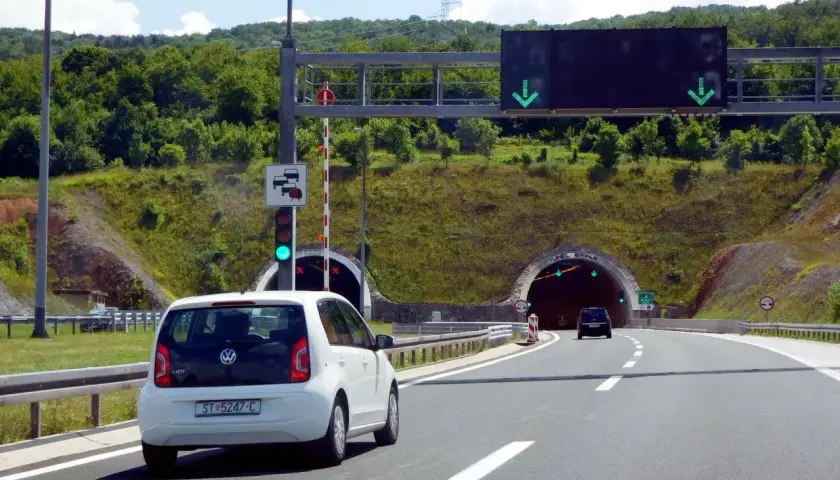 Biały samochód zbliża się do tunelu w Chorwacji. Znak drogowy informuje o opłatach za autostrady.